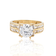 Gold ring with a large diamond and smaller diamonds on the band against a white background