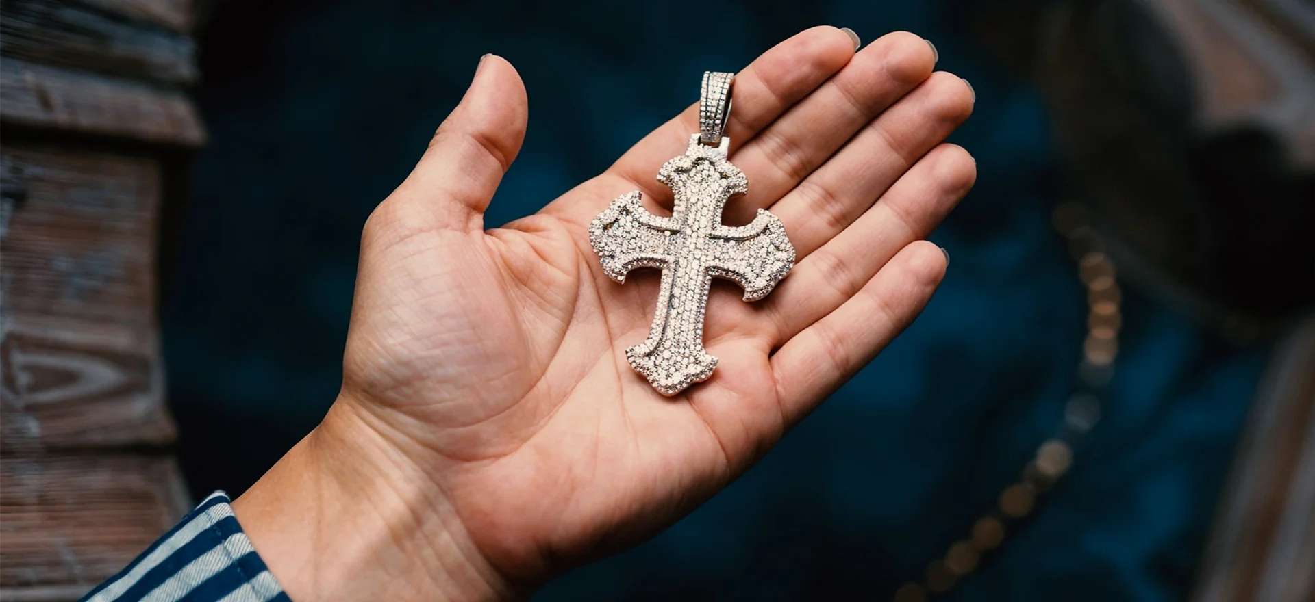 A hand holding a large, silver-toned Gothic cross pendant fully encrusted with shimmering stones.